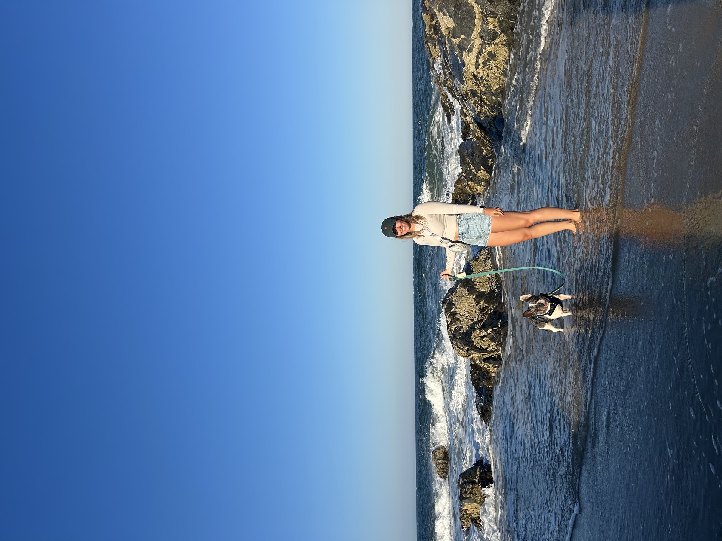 Sally holding Louie, her French Bulldog, on a rocky New England beach at golden hour